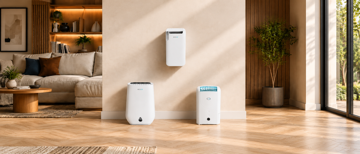 Three white portable air purifiers in different sizes displayed on a beige wall in a modern, sunlit living room with wood floors and a sofa.