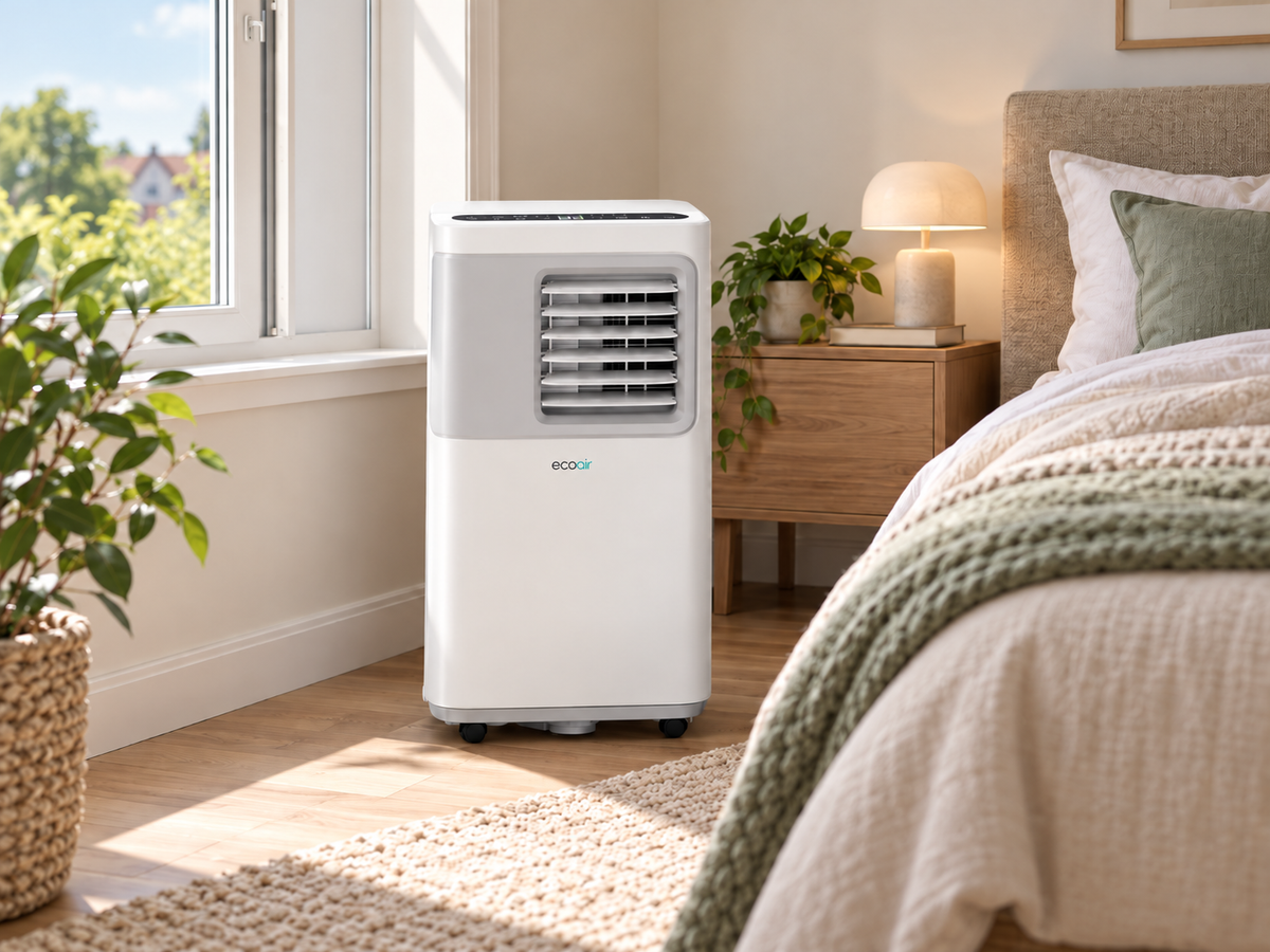 EcoAir portable air conditioner with wheels stands on a wooden floor in a bright, modern bedroom next to a bed and window.